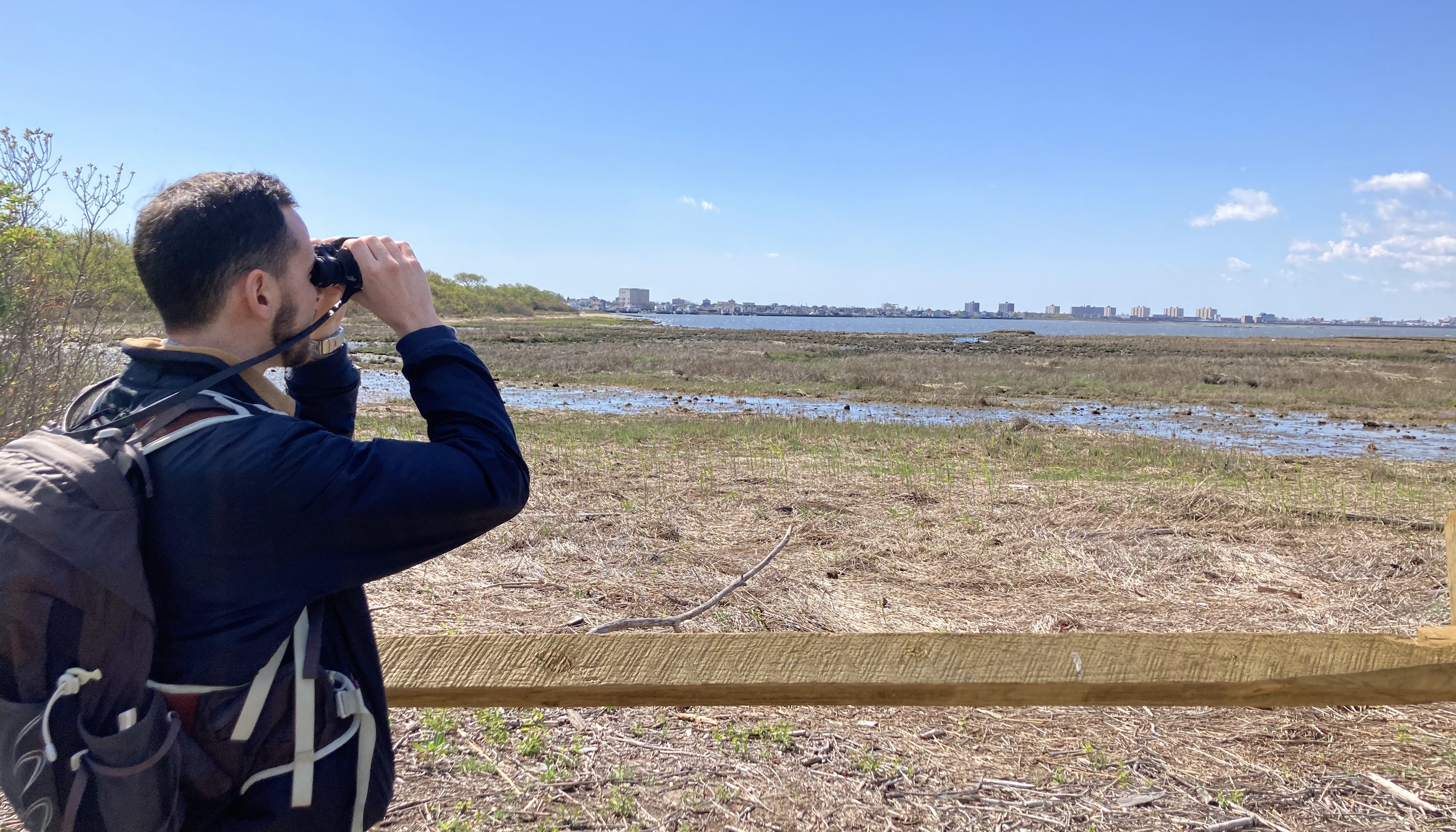 A person with binoculars stands overlooking the water.